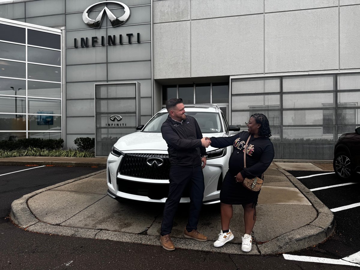 Two people standing beside a white Infiniti vehicle at a luxury car dealership showroom