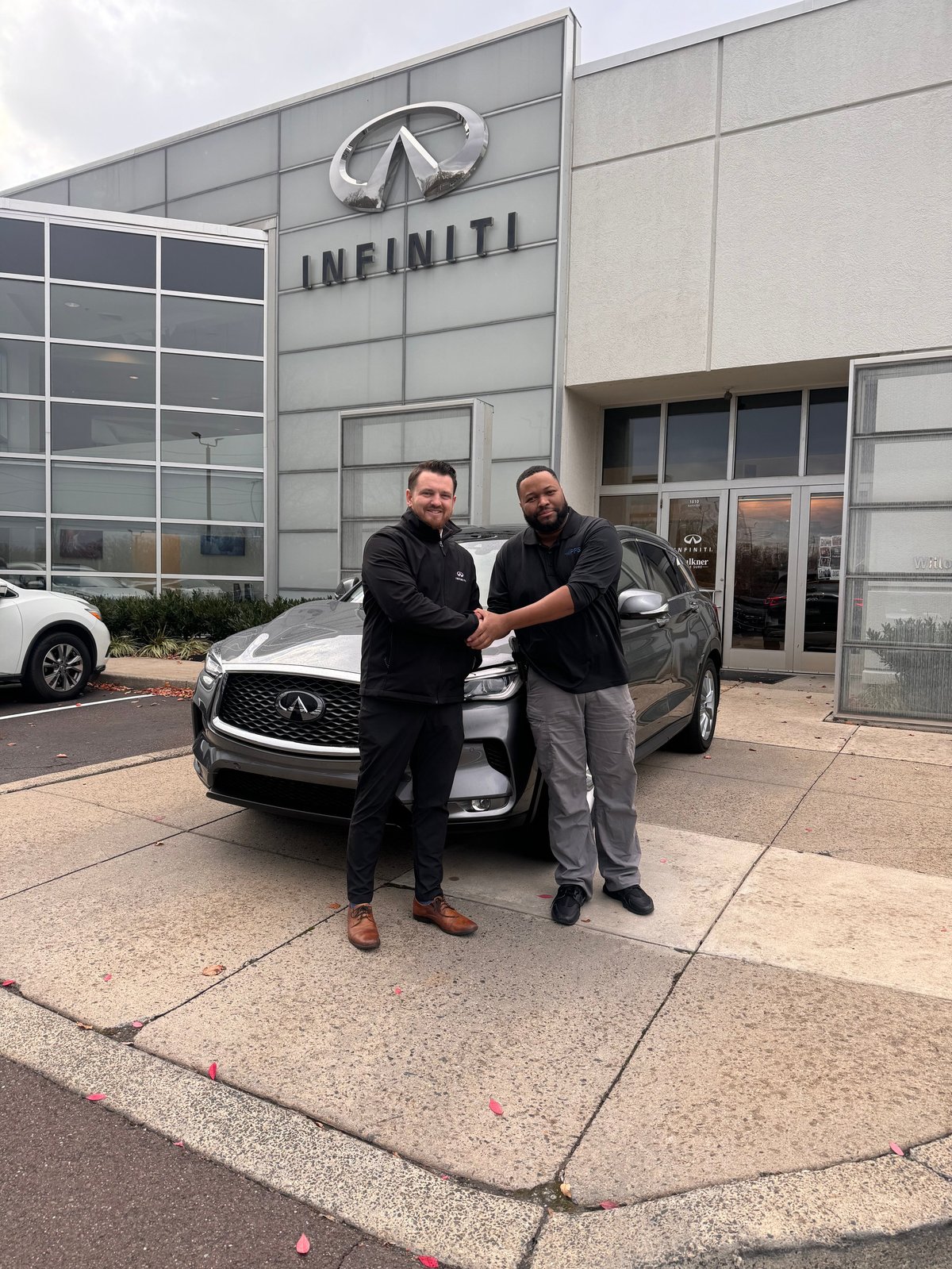 Two men shaking hands in front of a luxury INFINITI vehicle outside the INFINITI dealership at delivery